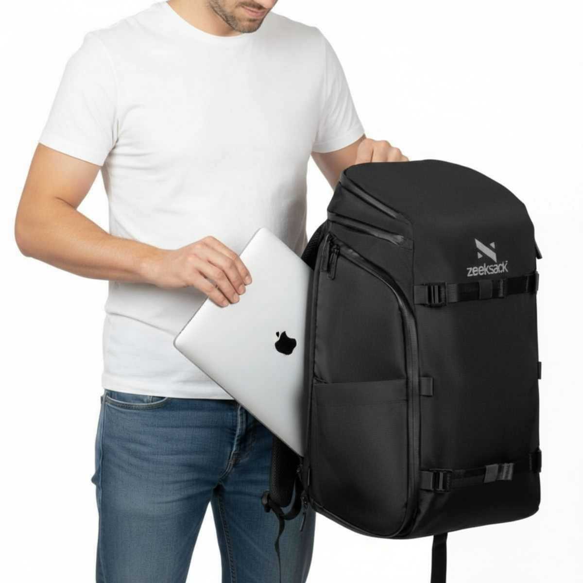 Man i vit t-shirt stoppar in en silvrig laptop i en svart ryggsäck.