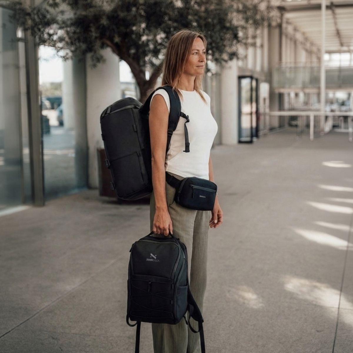 Zeeksack - Kvinna med The Organizer 30L på ryggen, The Underseat 15L i handen och Crossbody Organizer runt midjan.