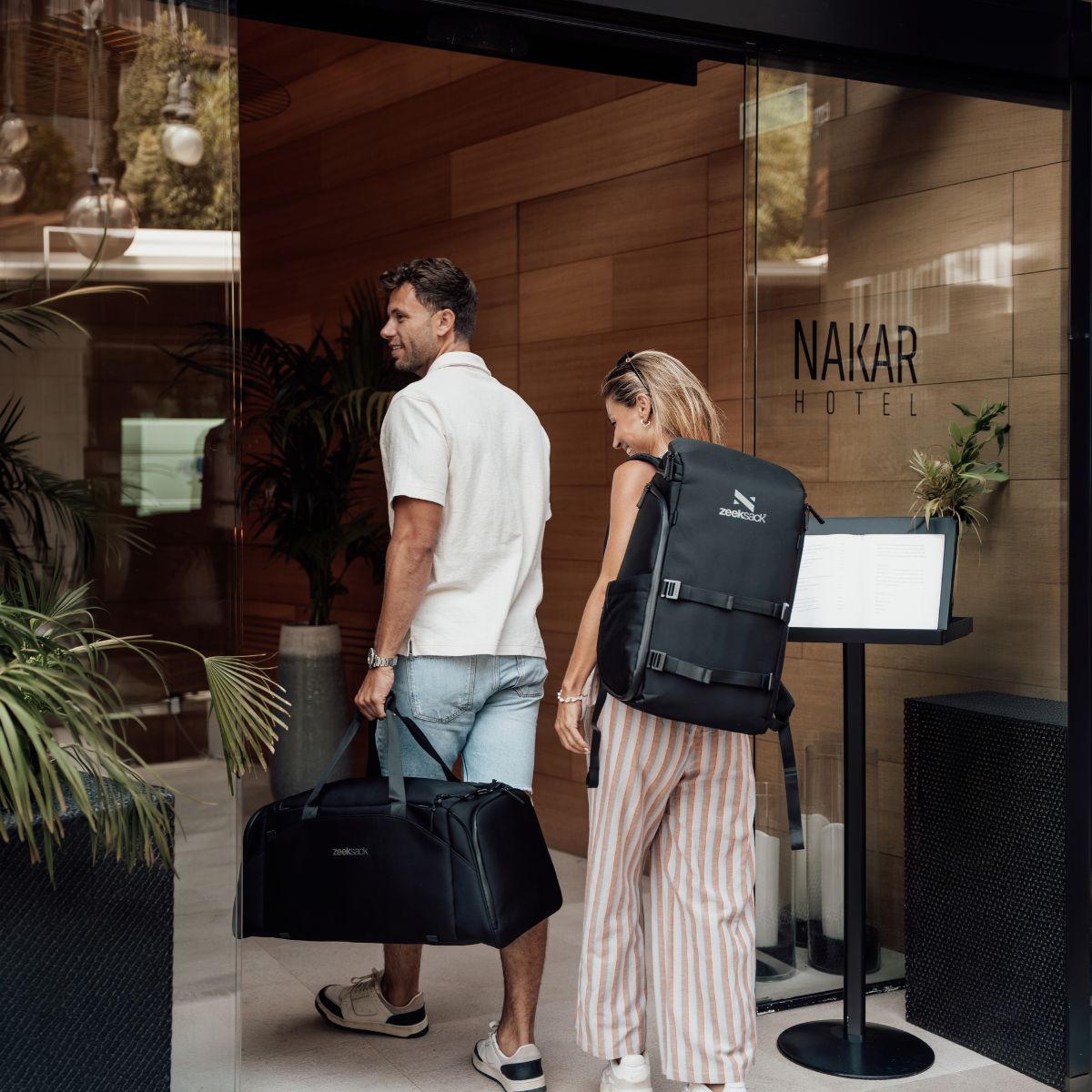 Zeeksack - Kvinna med The Organizer 30L på ryggen och man med The Weekender 50L i handen på väg in på ett hotell.