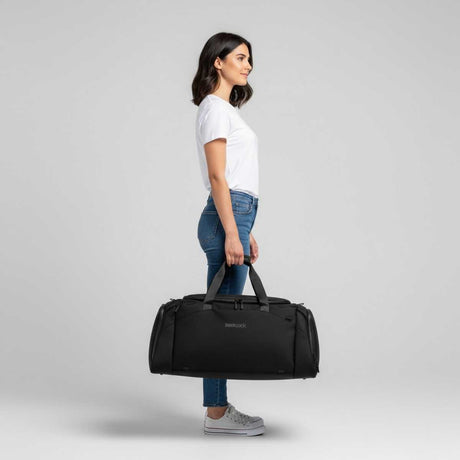 Kvinna i vit t-shirt och jeans håller en svart duffelbag i handen.